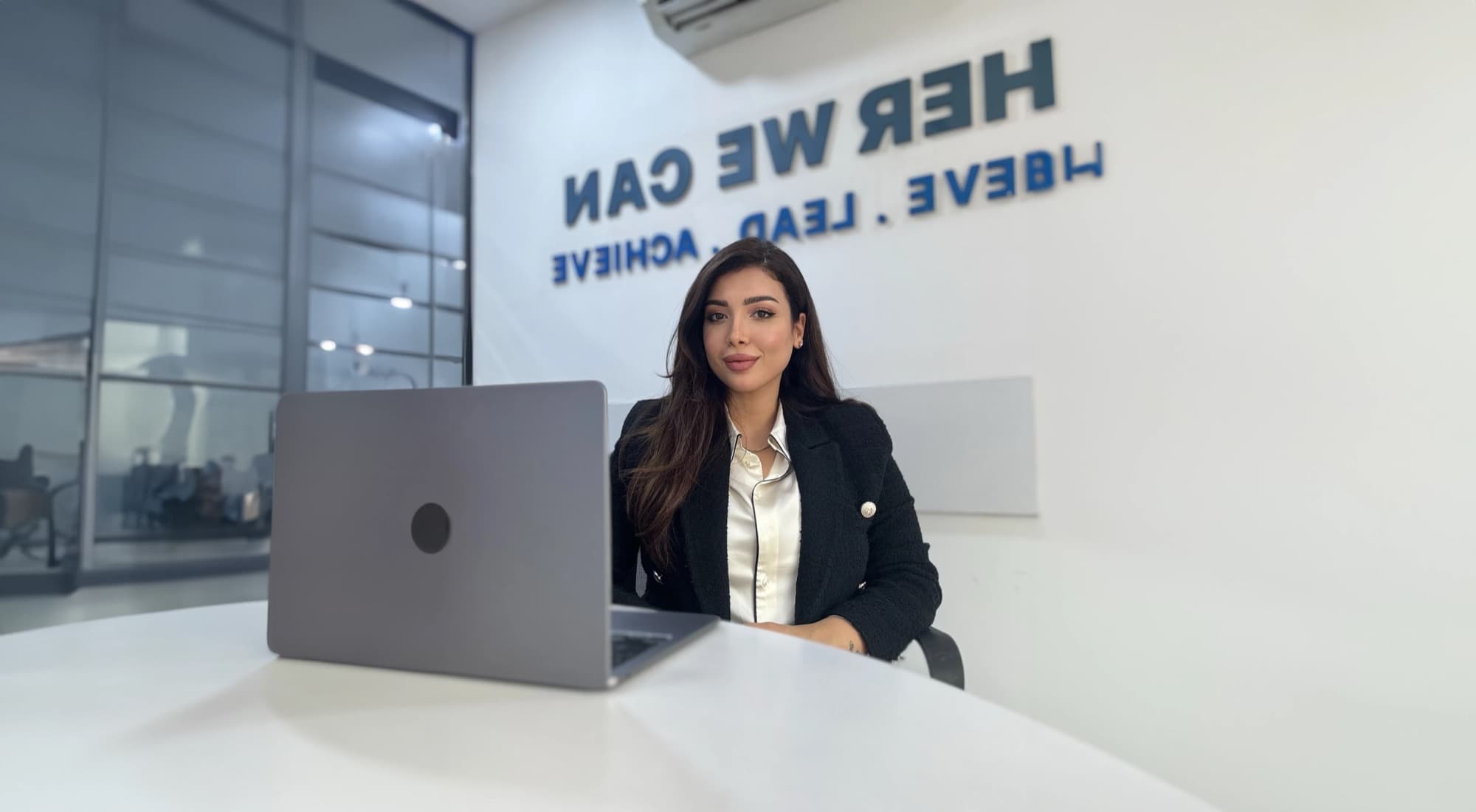 Walaa Mutar working at a laptop in front of a wall reading Here we can achieve, lead, achieve